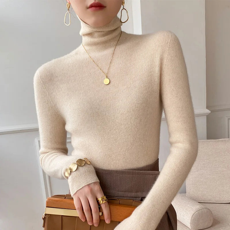 Slim-fit beige cashmere turtleneck sweater with ribbed texture, worn with gold jewelry and a brown skirt.
