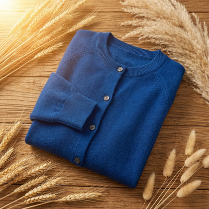Blue Merino wool cardigan with a classic button-up front, folded on a rustic wooden table with dried wheat stalks.