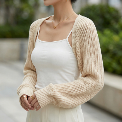 Beige ribbed knit cropped shrug with raglan sleeves worn over a white camisole for lightweight layering.