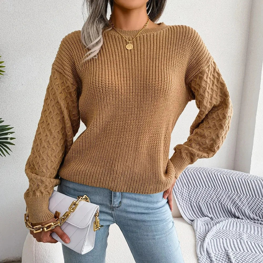 Person wearing a brown cable knit sweater and light blue jeans, holding a white handbag.